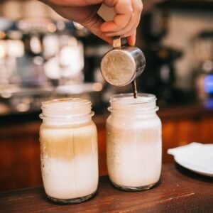 hand holding stainless steel cup pouring coffee on glass jars